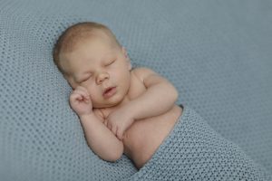 Babyfotograf Hamburg - Baby liegt auf der Seite schlafend zugedeckt mit einer blauen Decke