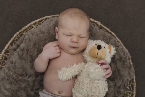 Babyfotograf Hamburg - Baby mit Teddy im Arm liegt schlafend im Körbchen