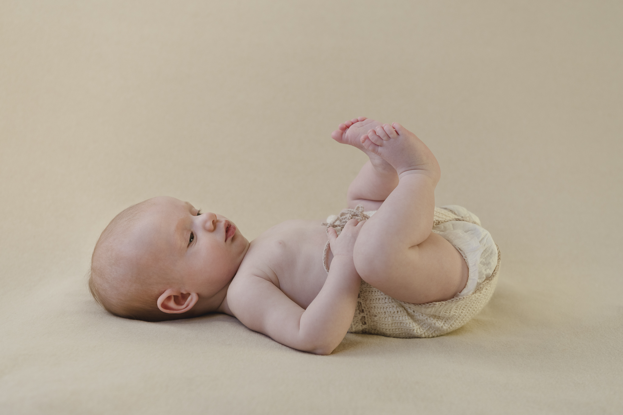 Babyfotoshooting - Baby liegt auf dem Rücken und spielt mit seinen Füßen