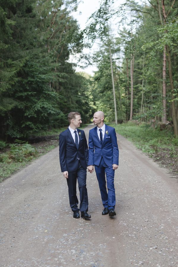 Hochzeitsfotograf Hamburg - schwules Brautpaar geht Hand in Hand einen Waldweg entlang
