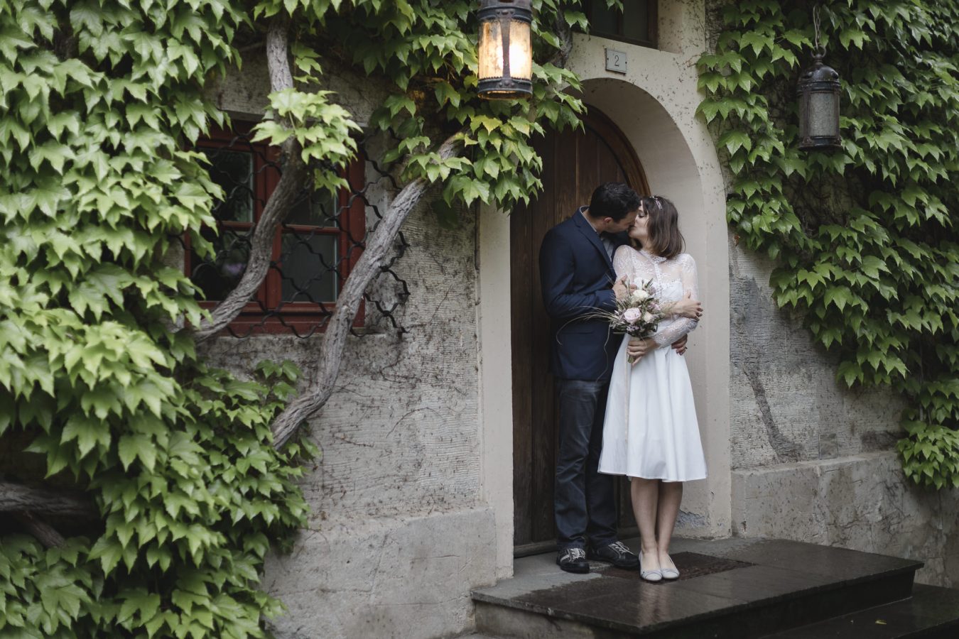 Hochzeit im Regen - Paar steht vor Haustür und küsst sich