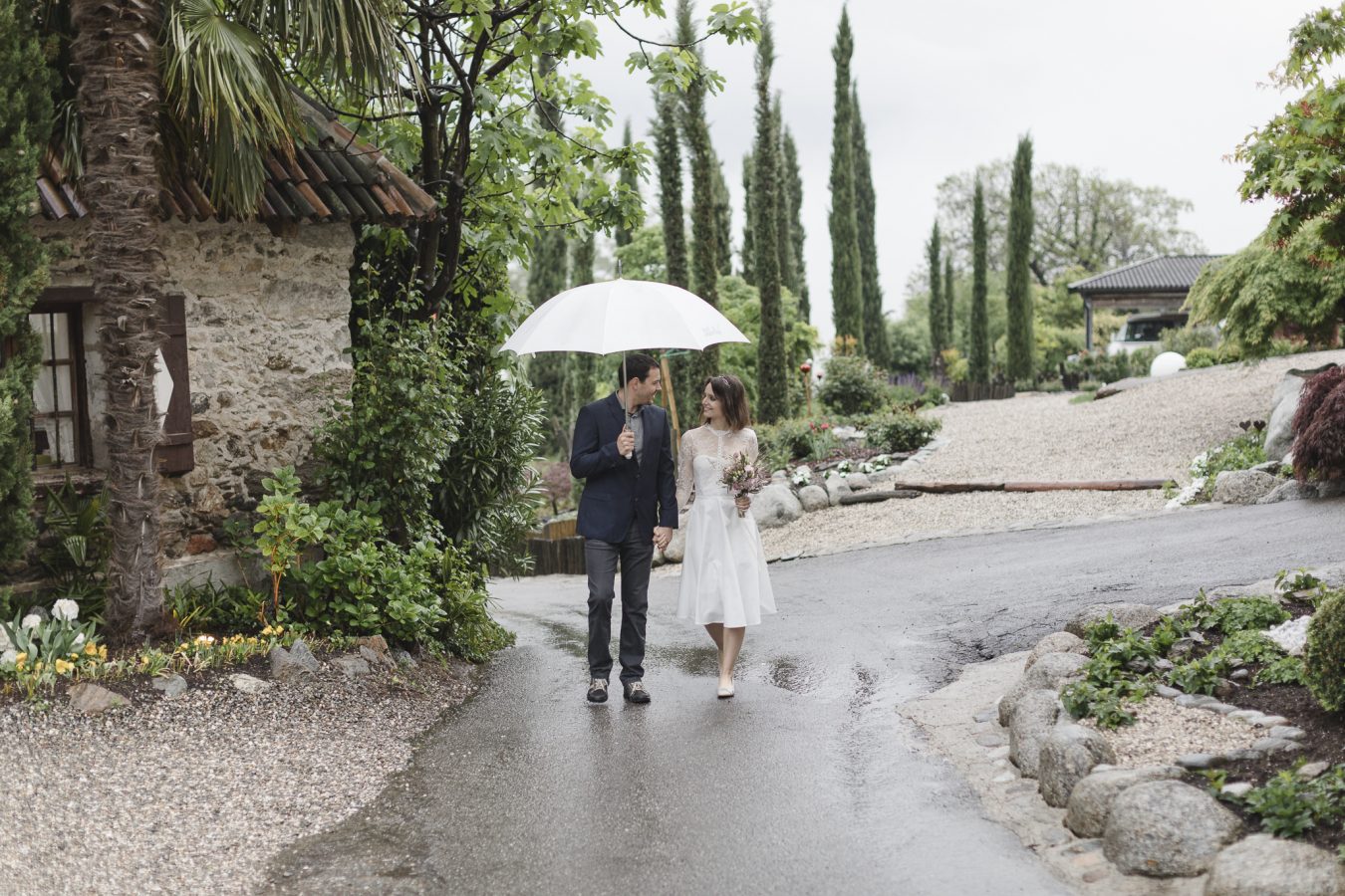 Hochzeit im Regen - Paar läuft mit Schirm einen Weg entlang