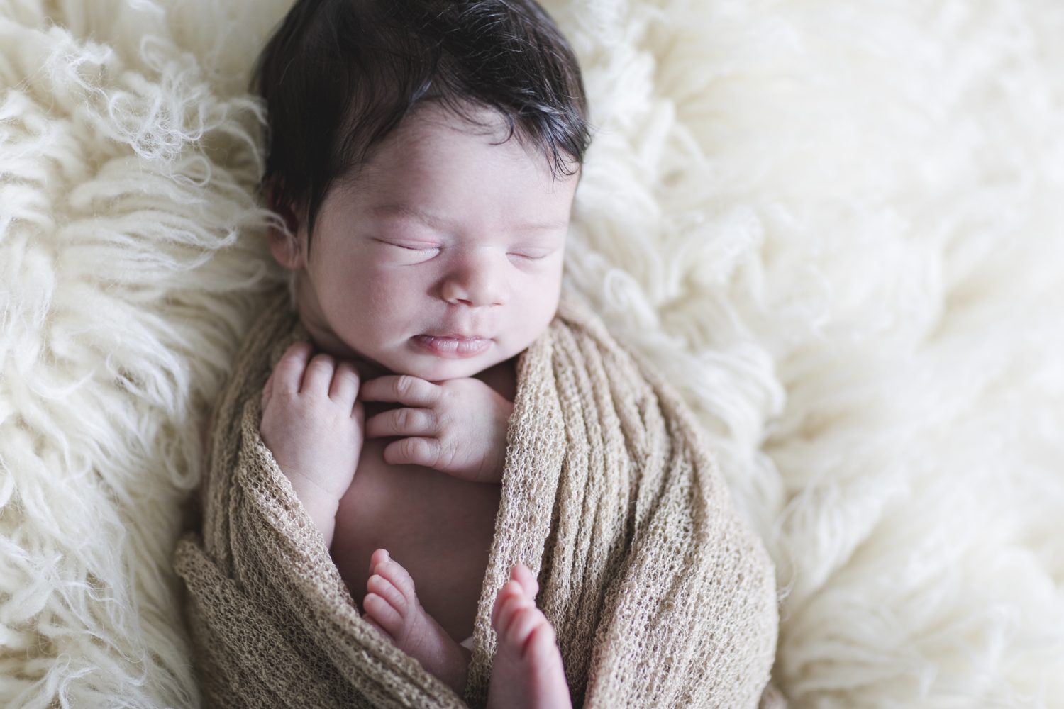 Babyfotograf Hamburg - Baby liegt in ein Tuch gewickelt auf einem Flokati