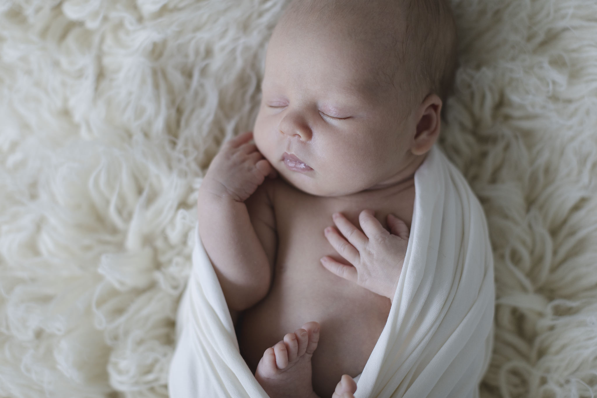 Babyfotograf Hamburg - Baby liegt in Wrap eingewickelt auf einem Flokati