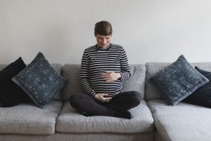 Babyfotograf Hamburg - Schwangere sitzt auf dem Sofa und schaut lächelnd auf ihren Bauch