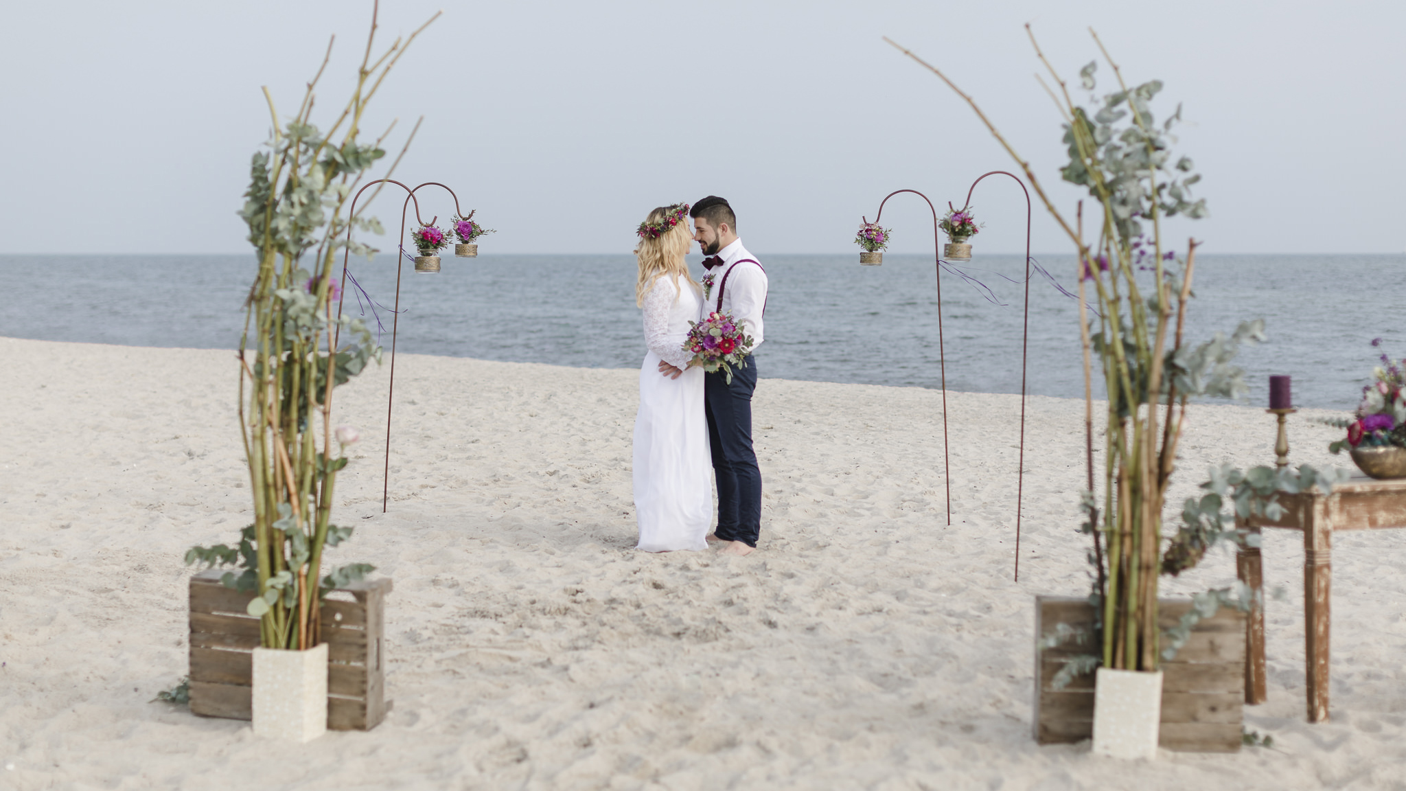 Strandhochzeit - Brautpaar steht im Blumenbogen und schaut sich verliebt an
