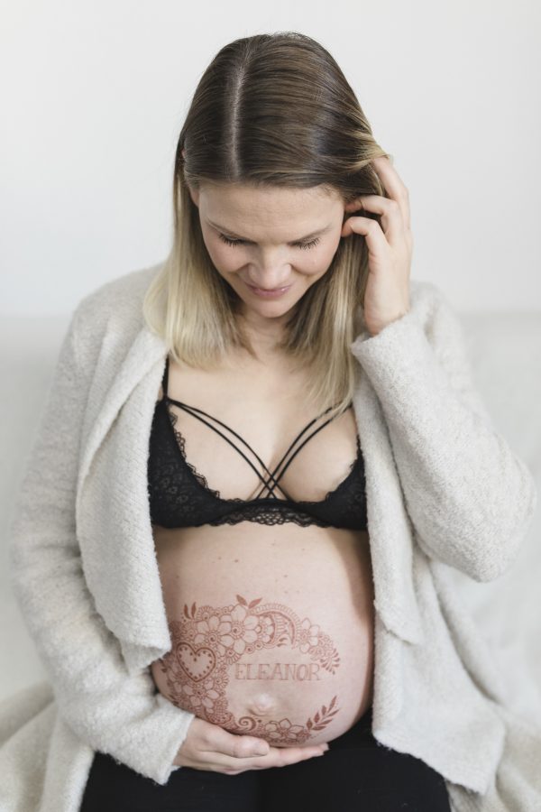 die Schwangere betrachtet ihr Henna Tattoo auf dem Babybauch